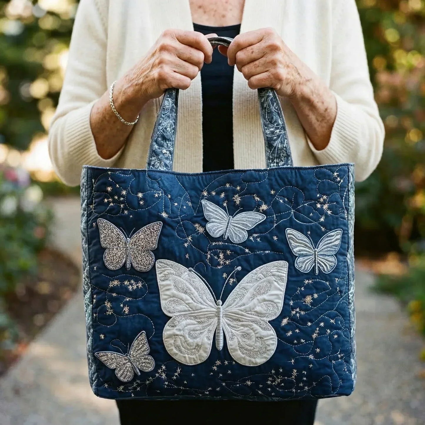 Handcrafted tote bag held open, dark navy quilted fabric with silver butterfly embroidery
