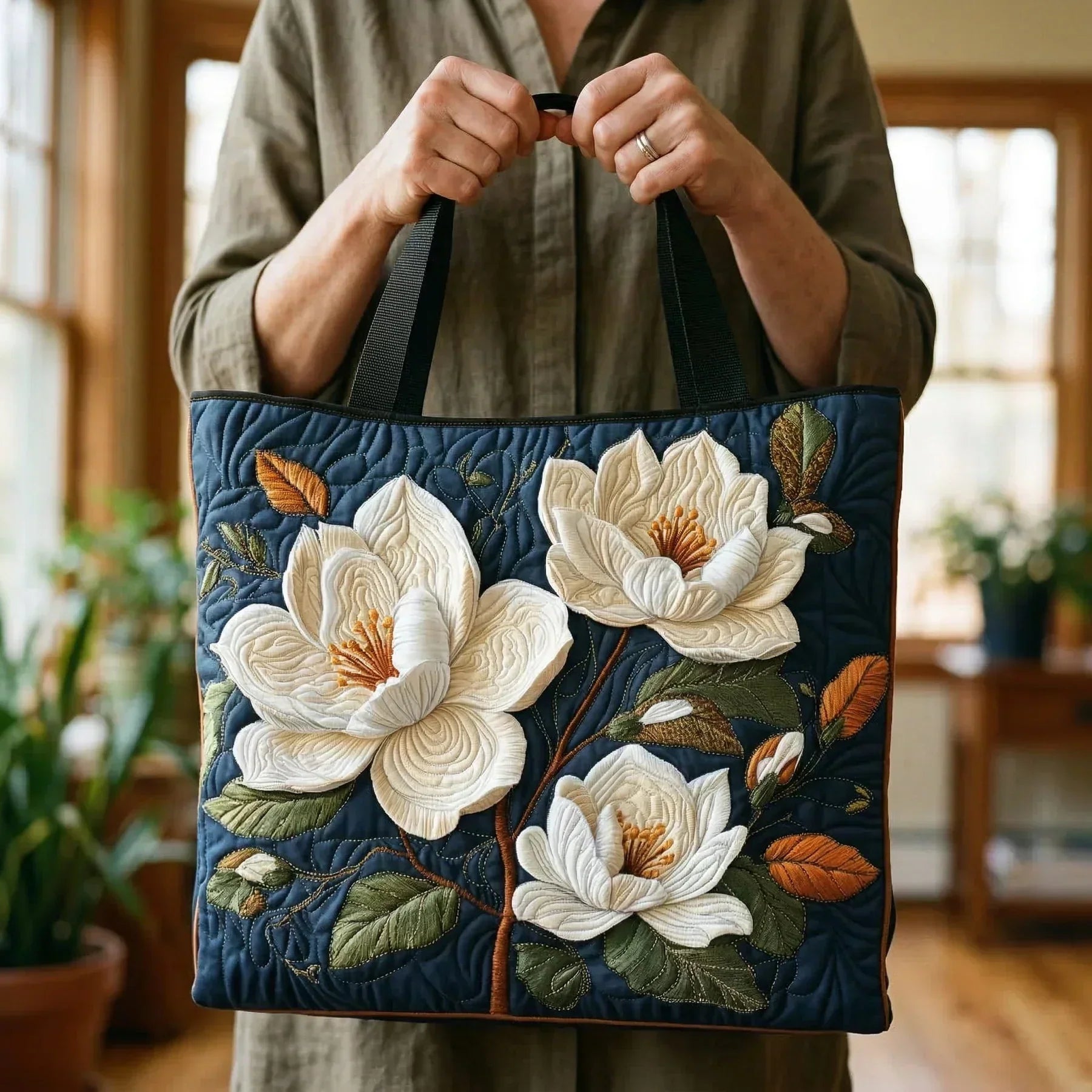 Quilted navy tote bag with white magnolia flowers, handles held upright