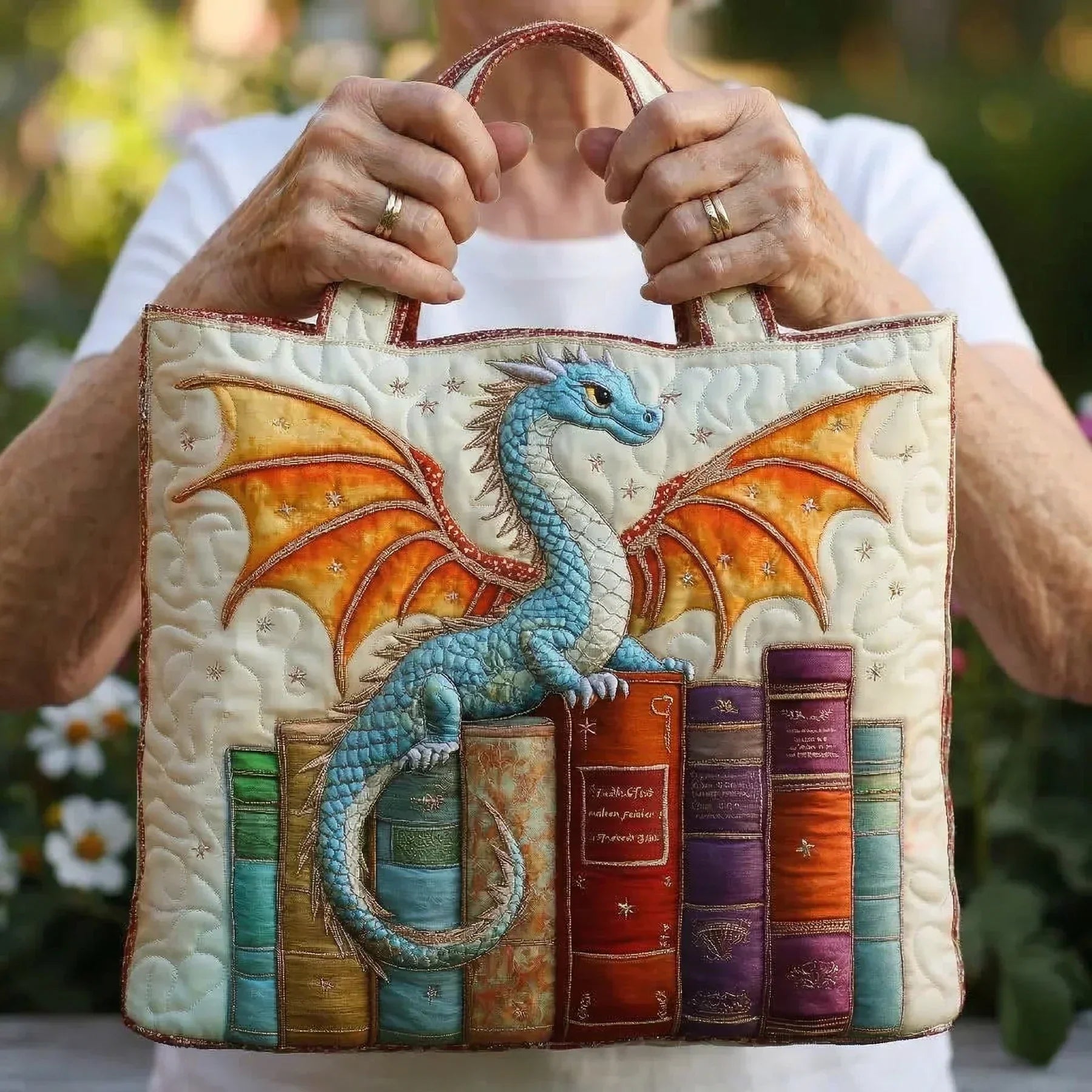 Quilted tote bag held by hands; blue dragon embroidery with colorful book panels