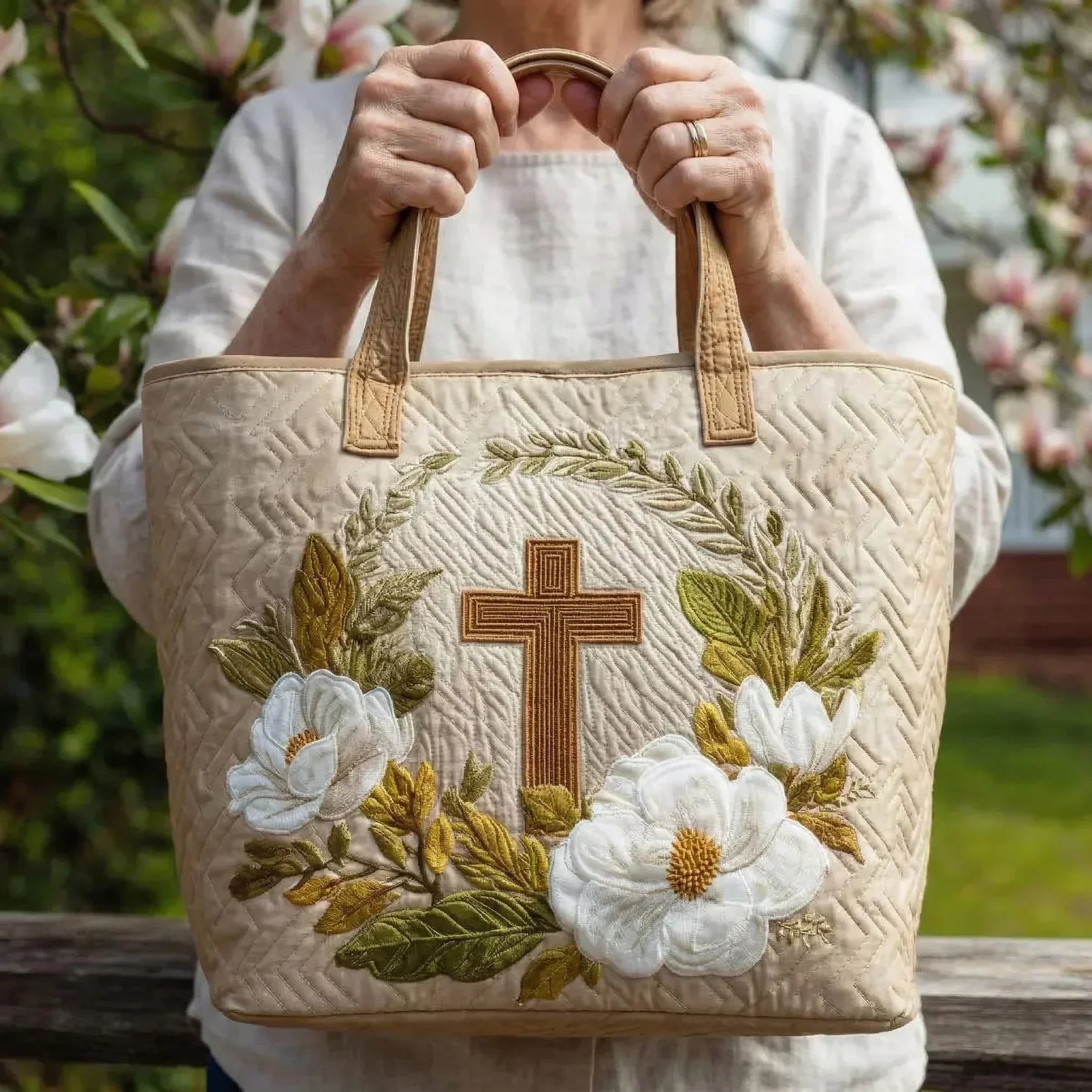 Beige embroidered tote bag with floral flowers and central cross; person holds the handles